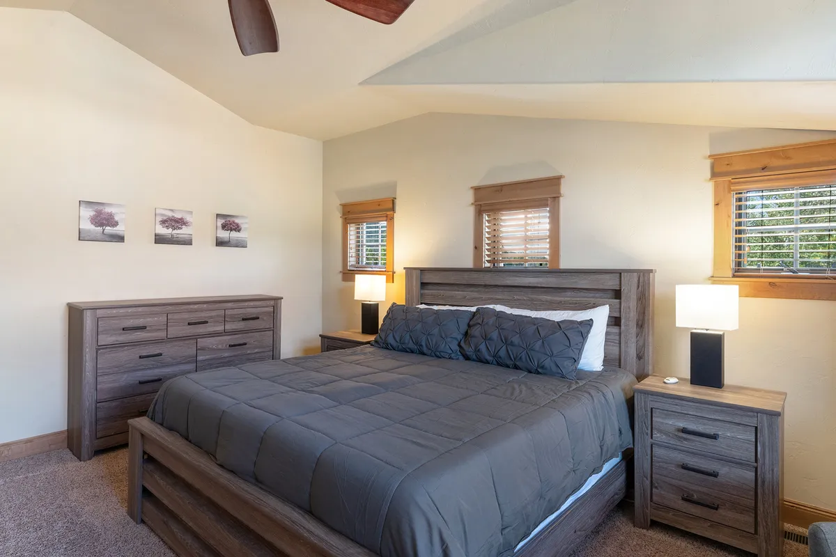 A peaceful bedroom scene featuring a comfortable bed, matching nightstands, a dresser, and generous window treatments that allow sunlight to fill the room. The space feels serene—ideal for restful sleep or focused work sessions.