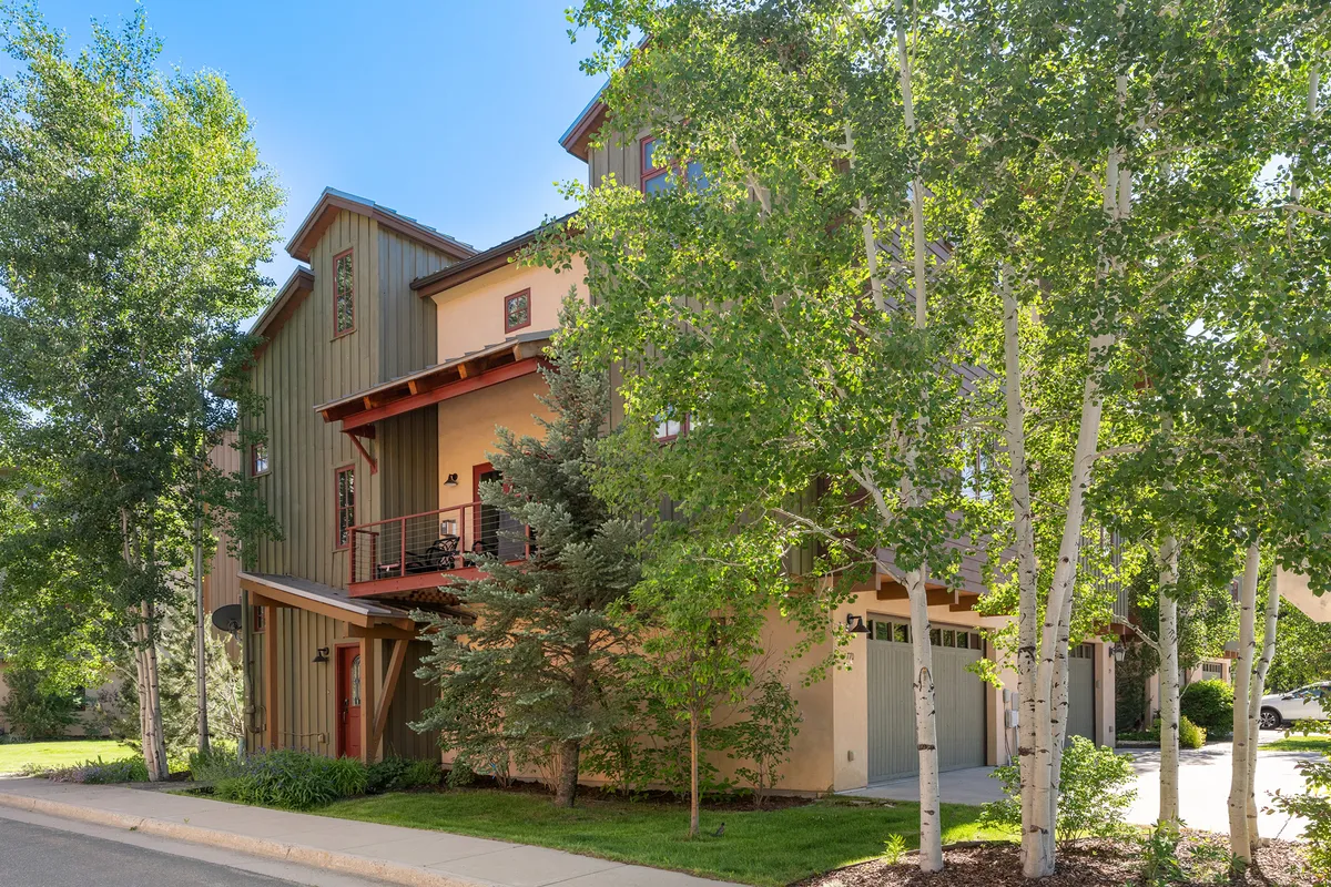 The image showcases the townhome’s modern facade nestled among graceful aspen trees, with a vibrant exterior, private balcony, and inviting outdoor spaces perfect for relaxing or socializing. The scene is set during golden hour, suggesting both tranquil mornings and warm, sunset gatherings.
