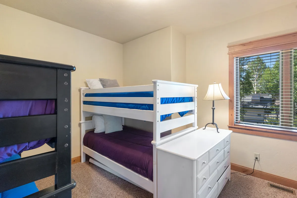 A cozy bedroom designed for children, with a bunk bed, dresser, and sunlight coming through the window. The space evokes a sense of fun and togetherness, perfect for sleepovers or quiet mornings after a day of activities.