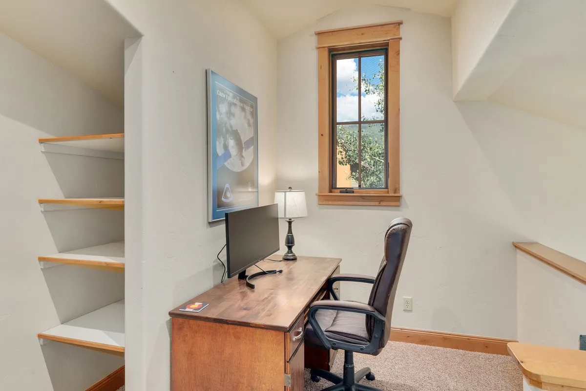 This image features a dedicated desk with a computer, a modern lamp, and a window allowing natural light to fill the workspace. The setup is minimalist and inviting, embodying a focused, serene atmosphere ideal for productivity.