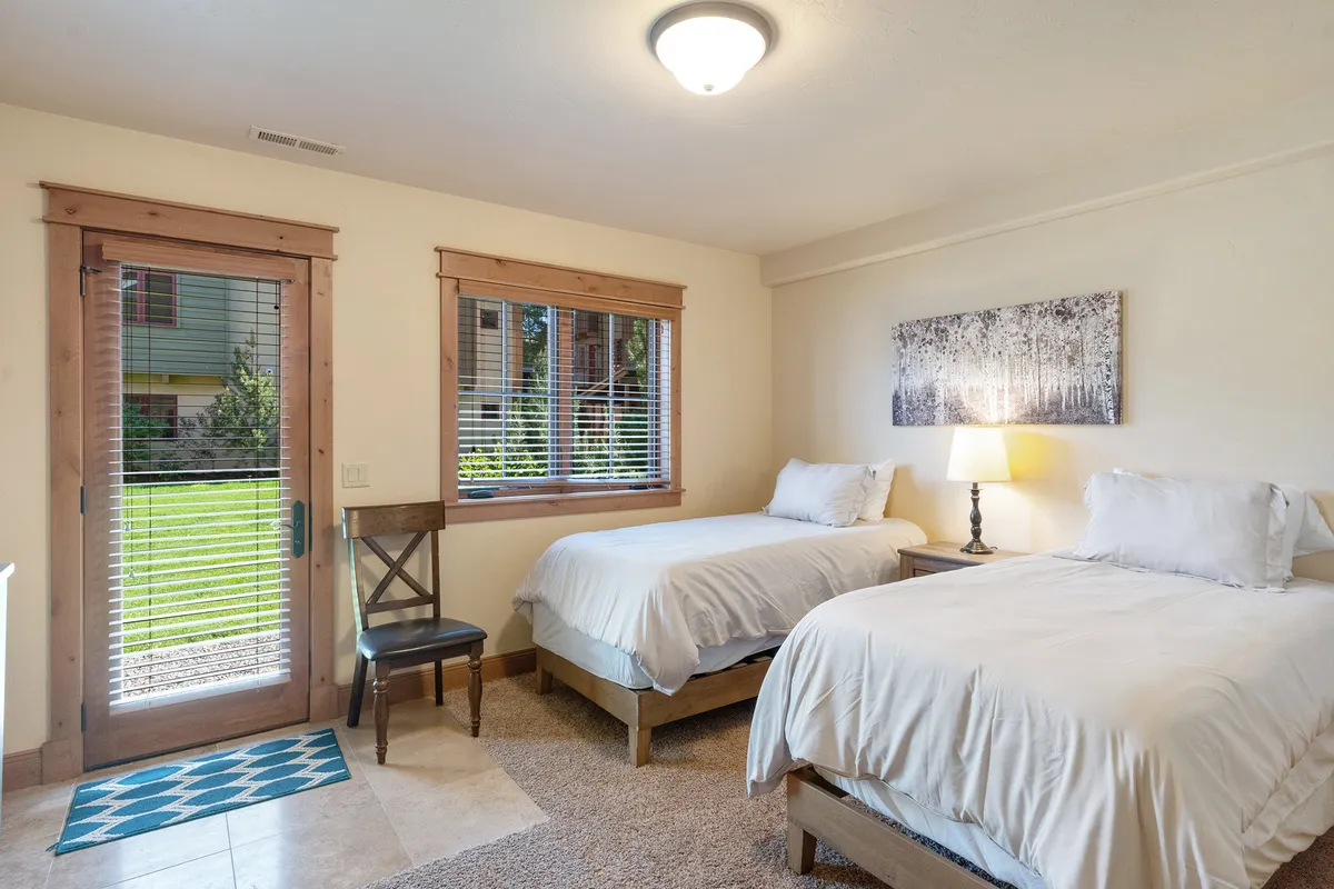 A serene bedroom with twin beds, a wooden chair, a lamp, and a window that offers a glimpse of the outside. The space is calm and functional, implying a relaxing retreat and potential easy storage for ski gear, in line with the section’s focus on convenience and rest after outdoor activities.
