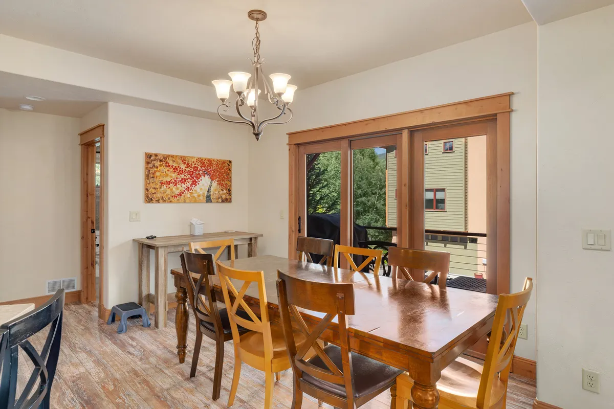A spacious dining area featuring a large table set beneath a striking chandelier. Natural light pours in through a sliding glass door, hinting at easy access to a deck or outdoor area—an ideal spot for family meals after outdoor adventures along the Yampa River.