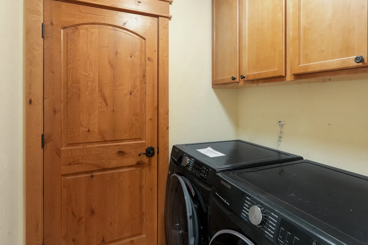 A well-organized laundry area with washing and drying machines, wooden cabinetry, and a sturdy wooden door. The space is bright and functional, suggesting ease in managing daily chores after outdoor activities, regardless of season.