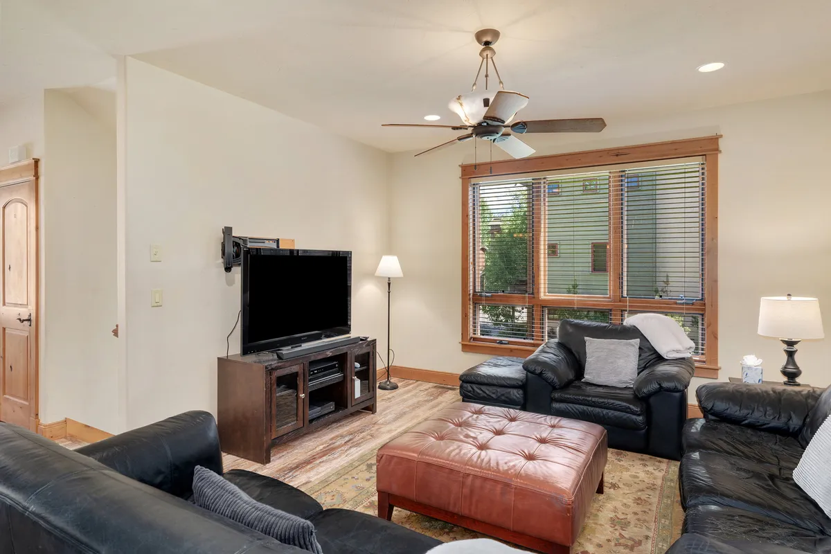 A cozy living area with a comfortable sofa, coffee table, television, and large windows. The space feels inviting and seamlessly transitions from work to relaxation, with ample natural light streaming in.