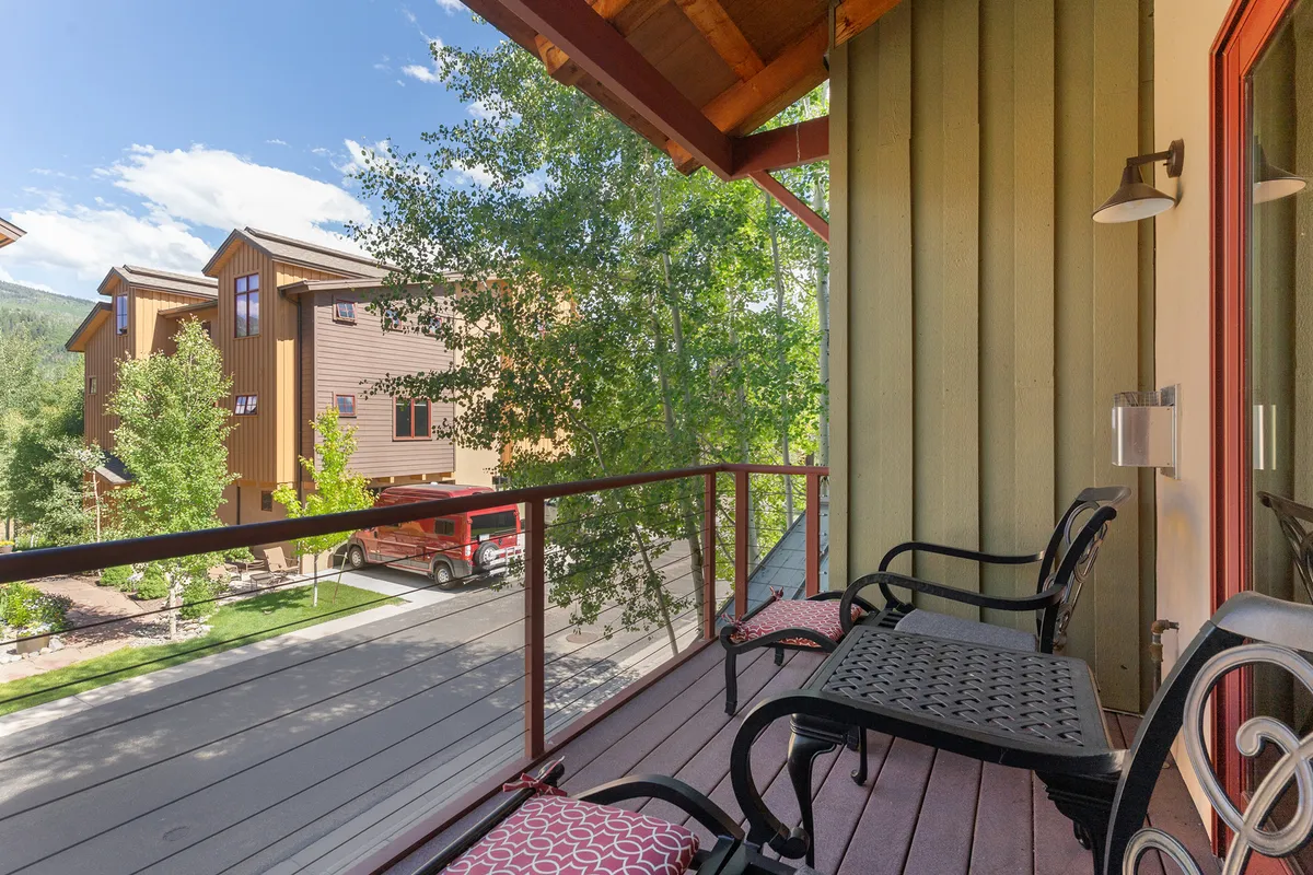 An exterior view of the balcony surrounded by trees, with seating that invites relaxation. The scene is tranquil, offering a glimpse of the outdoor environment that remote workers can step into for a refreshing break.